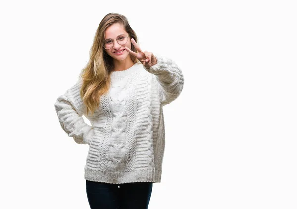 年轻美丽的金发女子穿着冬季毛衣和太阳镜在孤立的背景微笑着看着相机显示手指做胜利标志 第二个 — 图库照片