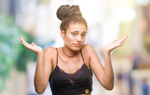 Young braided hair african american with pigmentation blemish birth mark over isolated background clueless and confused expression with arms and hands raised. Doubt concept.