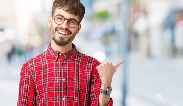 Seyir ve başparmak yanında yukarıyı mutlu yüz ile gülümseyen izole arka plan üzerinde gözlük takan genç yakışıklı adam.