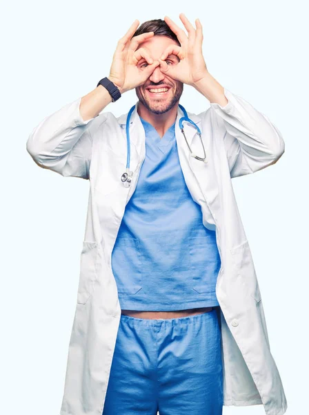 英俊的医生在孤立的背景上穿着医疗制服做确定的手势 比如双筒望远镜伸出舌头 眼睛透过手指看 疯狂的表达 — 图库照片