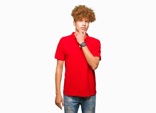 年轻的帅哥 头发是非洲的 穿着红色的 在镜头前看起来很自信 双臂交叉 双手举在下巴上 积极的思考 — 图库照片