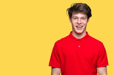 Yüz üzerinde mutlu ve serin bir gülümseme ile izole arka plan üzerinde kırmızı t-shirt giyen genç yakışıklı adam. Şanslı kişi.