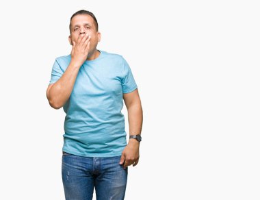 Orta yaş Arap adam izole arka plan üzerinde mavi t-shirt giyiyor yorgun esneme ağız ile elle kapsayan sıkılmış. Huzursuz ve uykululuk.