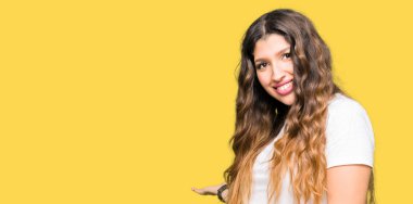 Açık el ile doğal gülümseyen girmek için rahat beyaz t-shirt davetkar giyen genç güzel kadın