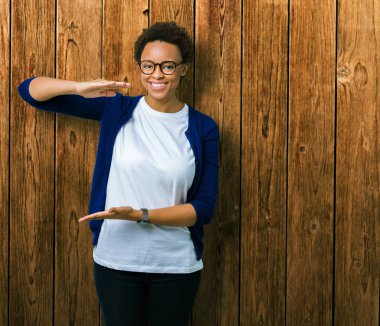 Büyük ve büyük boy işaret, ölçü birimi sembol gösteren ellerle eller izole arka plan üzerinde gözlük takan genç güzel Afrikalı-Amerikalı kadın. Kameraya bakarak gülümsüyordu. Ölçüm kavramı.