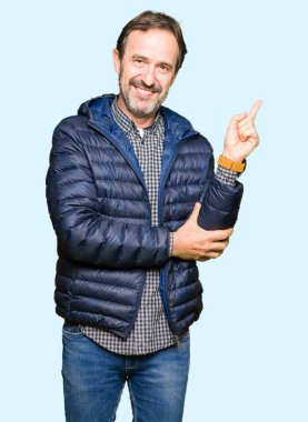 Kameraya bakarak yan el ve parmak ile işaret yüzünde, kocaman bir gülümseme ile kış ceket giyen orta yaş yakışıklı adam.