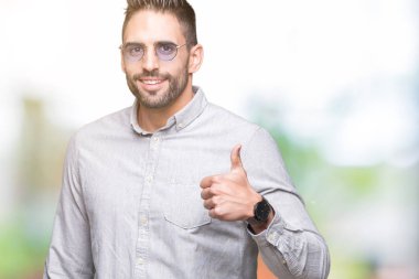 Genç yakışıklı adam hareketi el ile mutlu yaşasın yapıyor izole arka plan üzerinde güneş gözlüğü takıyor. Kameraya bakarak başarı gösteren ile ifade onaylama.