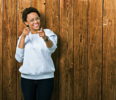 Fotoğraf makinesi ile mutlu ve komik yüz için parmakları işaret izole arka plan üzerinde gözlük takan genç güzel Afrikalı-Amerikalı kadın. İyi enerji ve vibes.