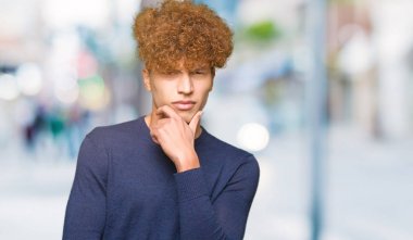 Yakışıklı genç afro saçlı emin çapraz kollar ve çeneme kaldırdı el ile gülümseme ile kameraya bakıyor. Pozitif düşünce.