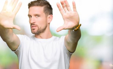 Yakışıklı adam çerçeve kullanarak yaparken rahat beyaz t-shirt gülen giyen eller avuç içi ve parmaklar, kamera perspektif