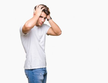Genç yakışıklı adam beyaz t-shirt giyiyor çünkü umutsuz ve stresli baş ağrısı acı izole arka plan üzerinde ağrı ve migren. Ellerini kafasına.