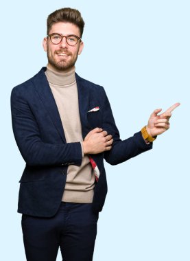 Kameraya bakarak yan el ve parmak ile işaret yüzünde, kocaman bir gülümseme ile gözlük takan genç yakışıklı iş adamı.