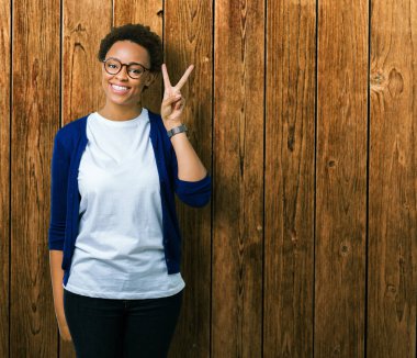 Genç güzel Afrikalı-Amerikalı kadın gözlük gösterilen ve parmakları ile işaret izole arka plan üzerinde kendinden emin ve mutlu gülümseyerek iken ikincisi.