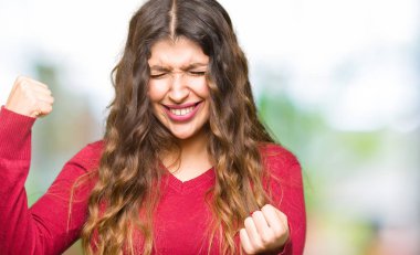 Gülümseyen ve başarı için çığlık kırmızı kazaklı çok mutlu ve heyecanlı kaldırdı, silah ile kazanan jest yapıyor giyen genç güzel kadın. Kutlama kavramı.