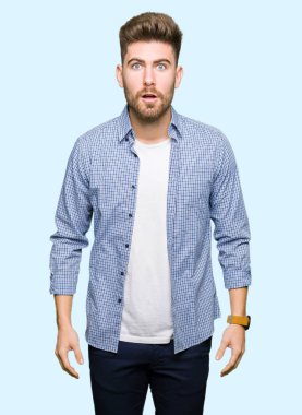 Genç yakışıklı sarışın adam rahat shirt korkuyor ve sürpriz ifade, korku ve heyecanlı yüz ile şok giyiyor.