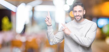 Gülümseyen ve iki elleri ve parmakları ile tarafına işaret kamera bakarak izole arka plan üzerinde sweatshirt giyen genç yakışıklı adam.