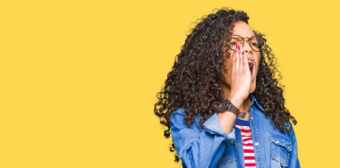 Kıvırcık saçlı Genç güzel kadın gözlük bağırıyor ve ağzına el ile yan gürültülü çığlık giyiyor. İletişim konsepti.