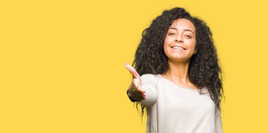 Kıvırcık saç ile genç güzel kız rahat kazak tebrik ve davetkar olarak dost sunan el sıkışması gülümseyen giyiyor. Başarılı iş.