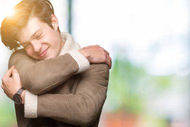 Genç yakışıklı kendini mutlu ve olumlu sarılma, kendinden emin gülümseyen izole arka plan üzerinde kış ceket giyen adam. Kendi aşk ve öz bakım