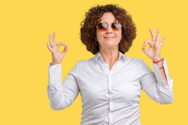 Güzel orta ager üst düzey iş kadın giyiyor güneş gözlüğü izole arka plan üzerinde dinlenmek ve gülümseyen gözlerle kapalı parmak jestle meditasyon yapıyor. Yoga kavramı.