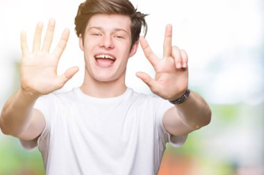 Gösterilen ve parmakları ile işaret izole arka plan üzerinde rahat beyaz t-shirt giyen genç yakışıklı adam kendinden emin ve mutlu gülümseyerek süre sekiz numara.