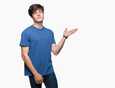 Neşeli sunulması ve kameraya bakarak avucunun ile işaret gülümseyen izole arka plan üzerinde mavi t-shirt giyen genç yakışıklı adam.