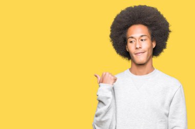 Seyir ve başparmak yanında yukarıyı mutlu yüz ile gülümseyen sportif sweatshirt giyen afro saçlı genç Afro-Amerikan adam.