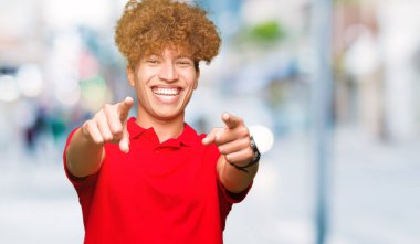 Olumlu ve neşeli gülümseyen kırmızı t-shirt işaretleme ve parmaklar, kamerayla giyen afro saçlı genç yakışıklı adam