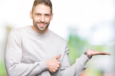 İzole arka plan gösteren palm el kazak giyen ve yukarıya, mutlu ve neşeli gülümseyen baş parmakları Tamam jest yapıyor yakışıklı delikanlı