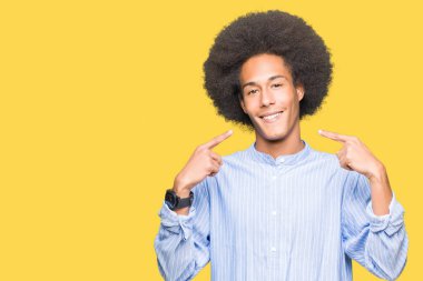 Afrikalı-Amerikalı genç afro saçlı emin gösterilen ve işaret parmakları diş ve ağız ile gülümseyen. Sağlık kavramı.