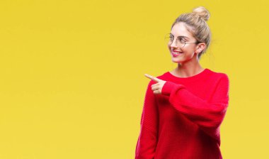 Kırmızı kazak ve gözlük izole arka neşeli bir gülümseme ile el ve parmak kadar kameraya bakarak yüzündeki mutlu ve doğal ifade ile yan ile işaret yüz üzerinde giyen genç güzel sarışın kadın.