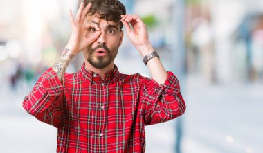 Sürpriz yüz, göz parmaklarının arasından seyir ile ok jest yapıyor izole arka plan üzerinde gözlüklü genç yakışıklı adam şok. İmansız ifade.