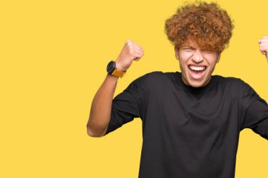 Çok mutlu ve heyecanlı kaldırdı, silah ile kazanan jest yapıyor gülümseyen ve başarı için çığlık siyah t-shirt giyen afro saçlı Genç yakışıklı adam. Kutlama kavramı.