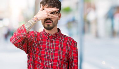 Mahcup ifadeyle parmaklarımın arasından seyir yüz ve gözler el ile kapsayan şok bakmak izole arka plan üzerinde gözlük takan genç yakışıklı adam.