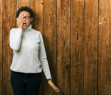 Yarım yüz, göz ve ağız el ile kapsayan yorgun esneme izole arka plan üzerinde gözlük takan genç güzel Afrikalı-Amerikalı kadın. Acı yüzü acıyor.