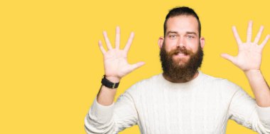 Kış kazak gösterme ve parmakları ile işaret giyen genç hipster adam kendinden emin ve mutlu gülümseyerek süre on numara.