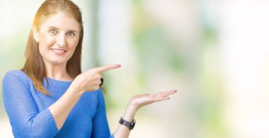 Hayret ve el ile sunulması ve parmak ile işaret ederken kameraya gülümseyen izole arka plan üzerinde kış kazak giyen güzel orta yaş Olgun kadın.