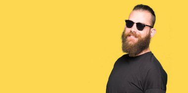 Genç hipster adam uzak tarafına yüzünde, doğal ifade gülümseme ile seyir güneş gözlüğü takıyor. Kendine güvenen gülüyor.