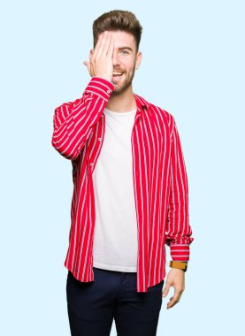 Yüz ve sürpriz duygu kendine güvenen gülümseme ile el ile bir göz kaplayan kırmızı gömlek giyen genç yakışıklı adam.