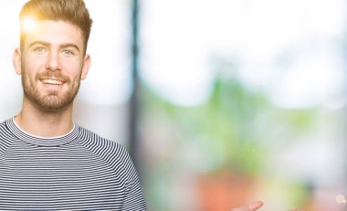 Hayret ve el ile sunulması ve parmak ile işaret ederken kameraya gülümseyen çizgili süveter giyen genç yakışıklı adam.