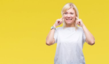 Yüksek sesle müzik gürültü rahatsız ifade parmaklarıyla kulaklarıyla kapsayan izole arka plan üzerinde beyaz t-shirt giyen genç güzel sarışın kadın. Sağır kavramı.