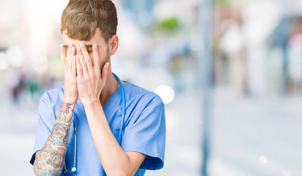 Young handsome nurse man wearing surgeon uniform over isolated background with sad expression covering face with hands while crying. Depression concept.
