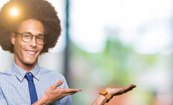 Young african american business man with afro hair wearing glasses Pointing to the side with hand and open palm, presenting ad smiling happy and confident