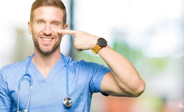 英俊的医生在孤立的背景上穿着医疗制服的人用手指指向脸和鼻子 面带微笑 — 图库照片