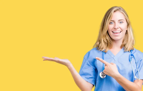 美丽的年轻医生妇女穿着医疗制服在孤立的背景惊讶和微笑的相机 而呈现与手和手指指指点点 — 图库照片