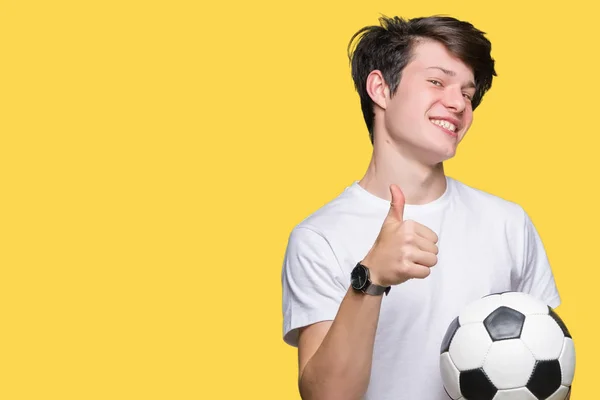 若い男が笑顔の サイン 優秀な兆候を親指をやって幸せな孤立した背景にサッカー サッカー ボールを保持 — ストック写真