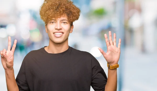 年轻的英俊男子与非洲头发穿着黑色的 T恤显示和手指指向 同时微笑着自信和快乐 — 图库照片