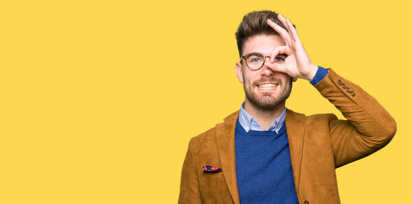 Young handsome business man wearing glasses doing ok gesture with hand smiling, eye looking through fingers with happy face.