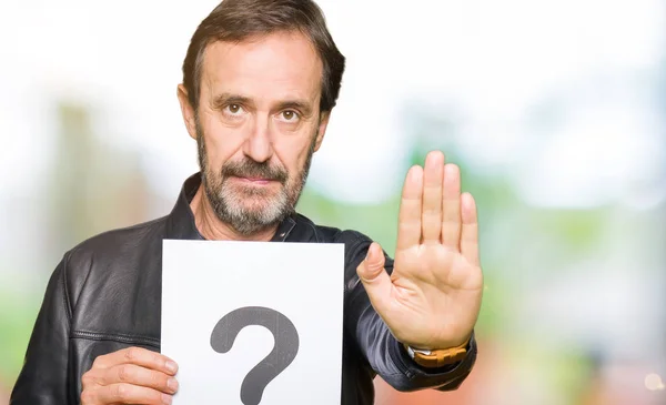 Handsome middle age man holding paper with question mark with open hand doing stop sign with serious and confident expression, defense gesture