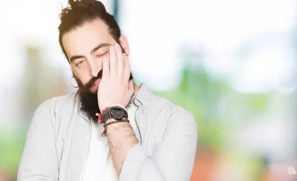 Young man with long hair, beard and earrings thinking looking tired and bored with depression problems with crossed arms.
